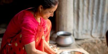 Harinas sin gluten para repostería india - GUSTOwebzine Mujer con un colorido sari rosa brillante corta verduras en una cocina exterior rústica, con boles de metal cerca.
