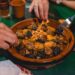 A spice vendor in Marrakech souk surrounded by colorful Moroccan cuisine ingredients