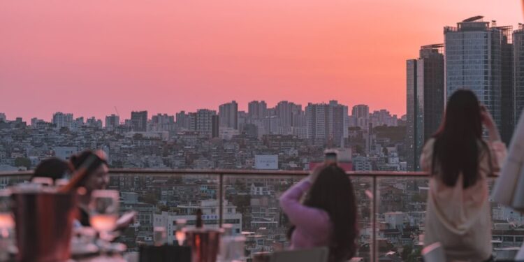 夕日の時間に、ピンク色のオレンジ色の空と都市のスカイラインを背景に、ルーフトップでの食事を楽しむ人々。