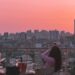 Menschen dinieren auf einem Dach bei Sonnenuntergang mit einem rosaorange Himmel über einer Stadtskyline.