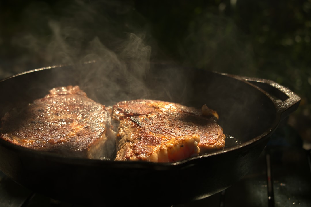A person sears a steak in a well-seasoned cast iron pan, showing the results of proper cast iron seasoning and maintenance.