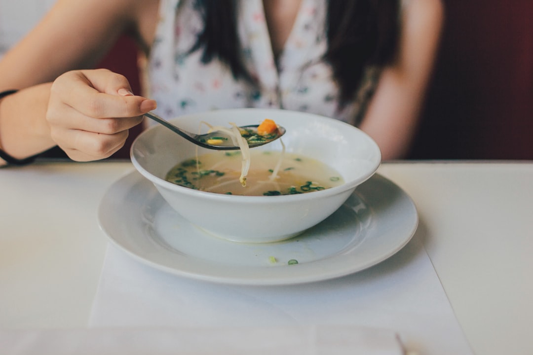 A server presenting a glass of chilled soups with garnish at a restaurant table