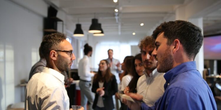 Club privati riservati ai soci a Singapore - GUSTOwebzine Gruppo di colleghi che si conoscono durante un evento in ufficio, alcuni con drink in mano e che chiacchierano in uno spazio aperto e luminoso con altri sullo sfondo.