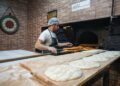 A man pressing flatbreads against the wall of a traditional clay oven, demonstrating the ancient craft of flatbread making.