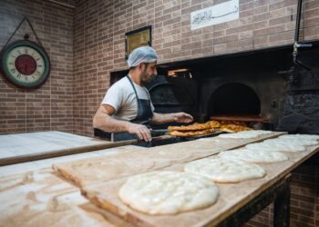 A man pressing flatbreads against the wall of a traditional clay oven, demonstrating the ancient craft of flatbread making.