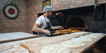 A man pressing flatbreads against the wall of a traditional clay oven, demonstrating the ancient craft of flatbread making.