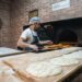 A man pressing flatbreads against the wall of a traditional clay oven, demonstrating the ancient craft of flatbread making.