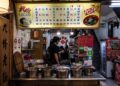 A woman carefully ladling street food pho broth into a bowl at a home kitchen counter