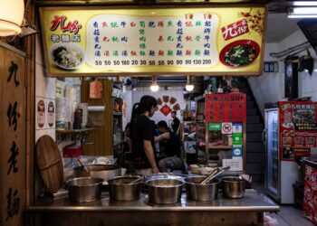 A woman carefully ladling street food pho broth into a bowl at a home kitchen counter