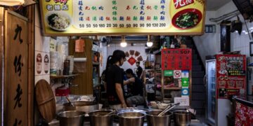 A woman carefully ladling street food pho broth into a bowl at a home kitchen counter
