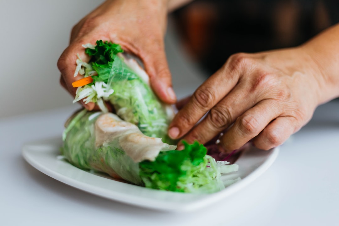 A woman assembling fresh spring rolls on a wooden board, recreating a classic Southeast Asian street food at home.