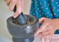 A woman grinding fresh cilantro and parsley in a mortar while preparing Moroccan chermoula from scratch