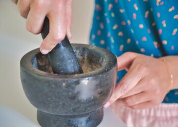 A woman grinding fresh cilantro and parsley in a mortar while preparing Moroccan chermoula from scratch