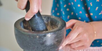 A woman grinding fresh cilantro and parsley in a mortar while preparing Moroccan chermoula from scratch