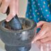 A woman grinding fresh cilantro and parsley in a mortar while preparing Moroccan chermoula from scratch
