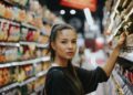 Woman shopping in a supermarket aisle, reaching to grab an item from the shelf.