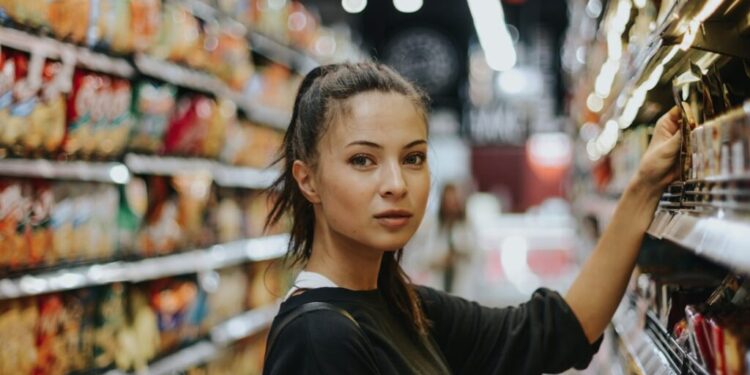 Woman shopping in a supermarket aisle, reaching to grab an item from the shelf.
