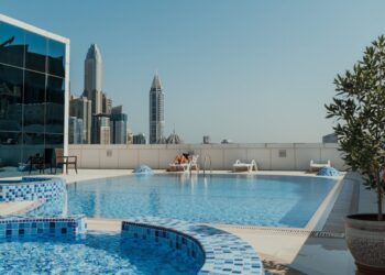 Rooftop swimming pool with blue mosaic tiles and a city skyline in the background under a clear blue sky