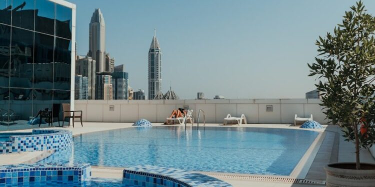 Luxus-Pools in Dubai zum Buchen diesen Sommer - GUSTOwebzine Dach-Swimmingpool mit blauen Mosaikfliesen und Skyline der Stadt im Hintergrund unter klarem blauem Himmel