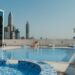 Rooftop swimming pool with blue mosaic tiles and a city skyline in the background under a clear blue sky