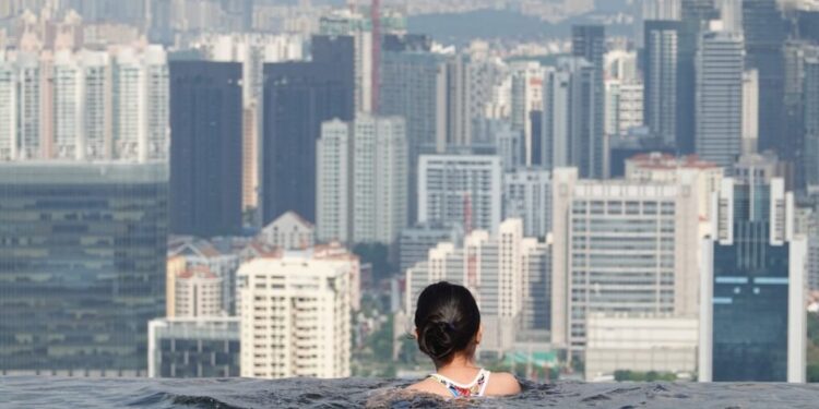Back view of a person with dark hair in an infinity pool, facing a dense city skyline.