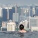 Back view of a person with dark hair in an infinity pool, facing a dense city skyline.