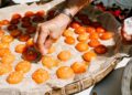 baker-pressing-apricots-into-tart-unsplash - GUSTOwebzine A pastry chef arranging halved apricots into a frangipane tart shell, showcasing the craft of stone fruit dessert preparation