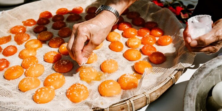 A pastry chef arranging halved apricots into a frangipane tart shell, showcasing the craft of stone fruit dessert preparation