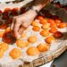 Un pasticcere che sistema le albicocche tagliate a metà in una crostata con crema di mandorle, mostrando l'artigianato della preparazione di dolci di frutta a nocciolo