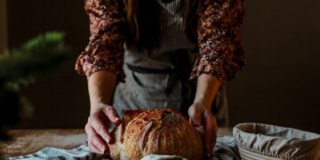 Wheat-free bread traditions across the EU - GUSTOwebzine Person in a floral blouse shapes a round rustic loaf of bread on a striped towel on a wooden table