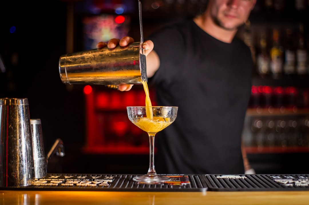 A bartender adding drinking vinegars to a cocktail glass filled with fresh summer fruit and ice
