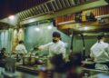A head chef studies a new autumn menu at a prep counter, preparing for the seasonal shift from summer to cooler months
