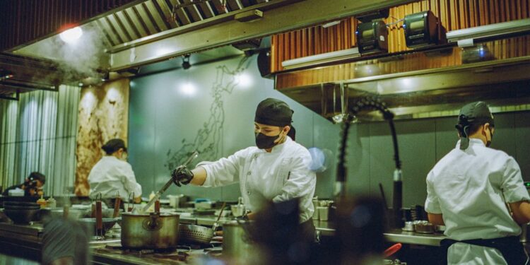 A head chef studies a new autumn menu at a prep counter, preparing for the seasonal shift from summer to cooler months