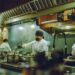 A head chef studies a new autumn menu at a prep counter, preparing for the seasonal shift from summer to cooler months