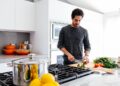 A professional chef finely chopping fresh parsley to prepare a classic green sauce at a wooden kitchen counter