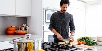 A professional chef finely chopping fresh parsley to prepare a classic green sauce at a wooden kitchen counter