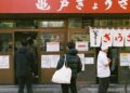 Singapore dining resets before September rush - GUSTOwebzine People stand in line outside a Japanese eatery with white curtain banners and red signage above the door, posters on the windows.