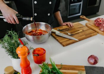Een chef-kok die de basis van een marinade, inclusief olie, citrus en verse kruiden, in een grote keramische kom mengt