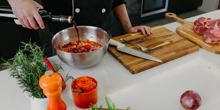A chef whisking together marinade basics including oil, citrus, and fresh herbs in a large ceramic bowl