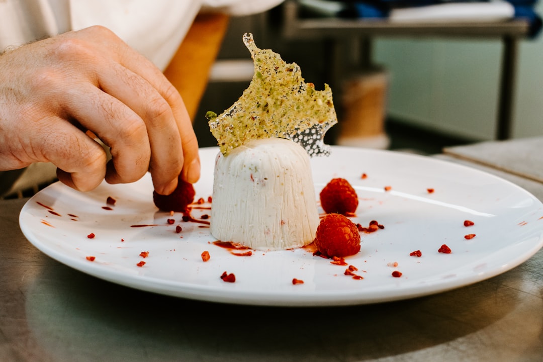 A chef carefully plating a chilled cherry stone fruit dessert with a spoon of cream in a small ceramic bowl.