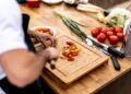 A person chopping multicolored cherry tomatoes on a wooden cutting board in a kitchen.