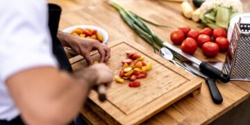 A person chopping multicolored cherry tomatoes on a wooden cutting board in a kitchen.