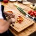 A person chopping multicolored cherry tomatoes on a wooden cutting board in a kitchen.