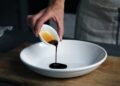 chef-pouring-aged-vinegar-dish-unsplash - GUSTOwebzine A chef carefully drizzling aged vinegar over a finished plate in a professional kitchen