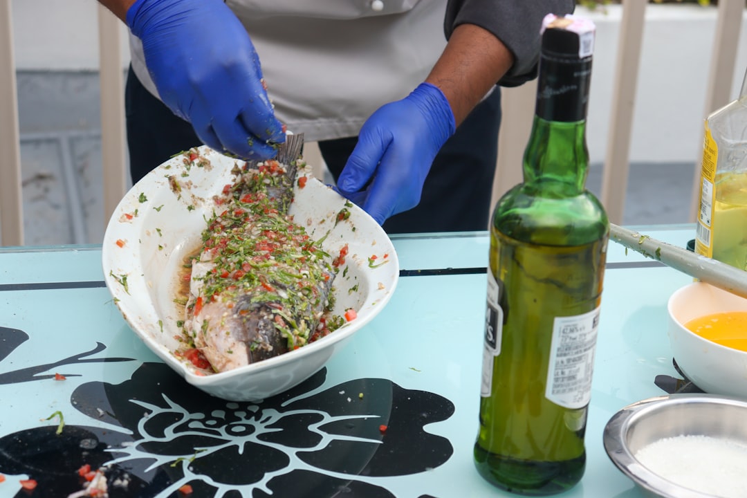 A cook spooning a vibrant homemade green sauce over a fillet of grilled fish on a white plate