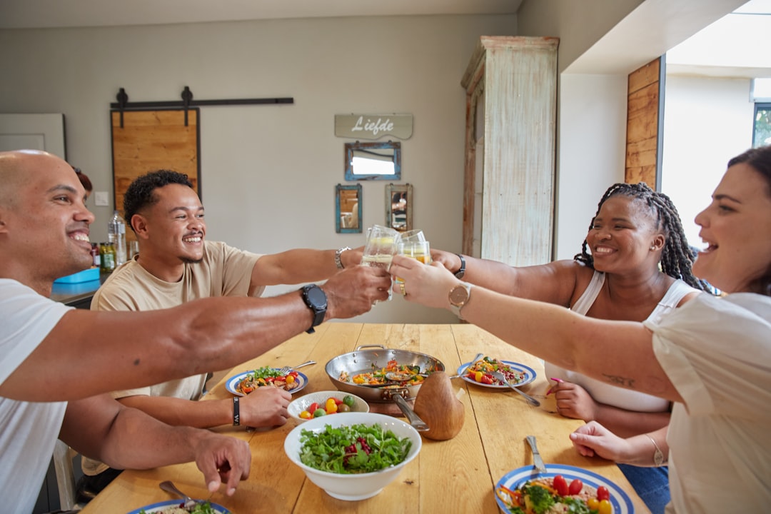 A diverse group of friends laughing and eating together at a long communal table set with multiple shared dishes.