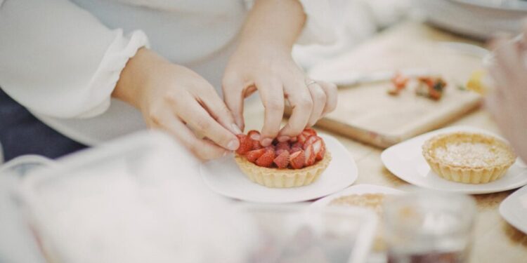 Close-up of hands decorating a strawberry tart with sliced berries on a white plate