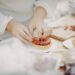 Close-up of hands decorating a strawberry tart with sliced berries on a white plate