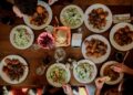 A group of guests reaching across a communal table covered in shared dishes, celebrating the communal table tradition.
