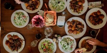 A group of guests reaching across a communal table covered in shared dishes, celebrating the communal table tradition.
